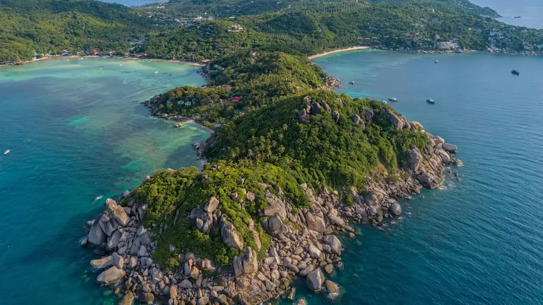 Vue aérienne d’une pointe rocheuse couverte de jungle, entourée de blocs de granit et de hauts-fonds turquoise.