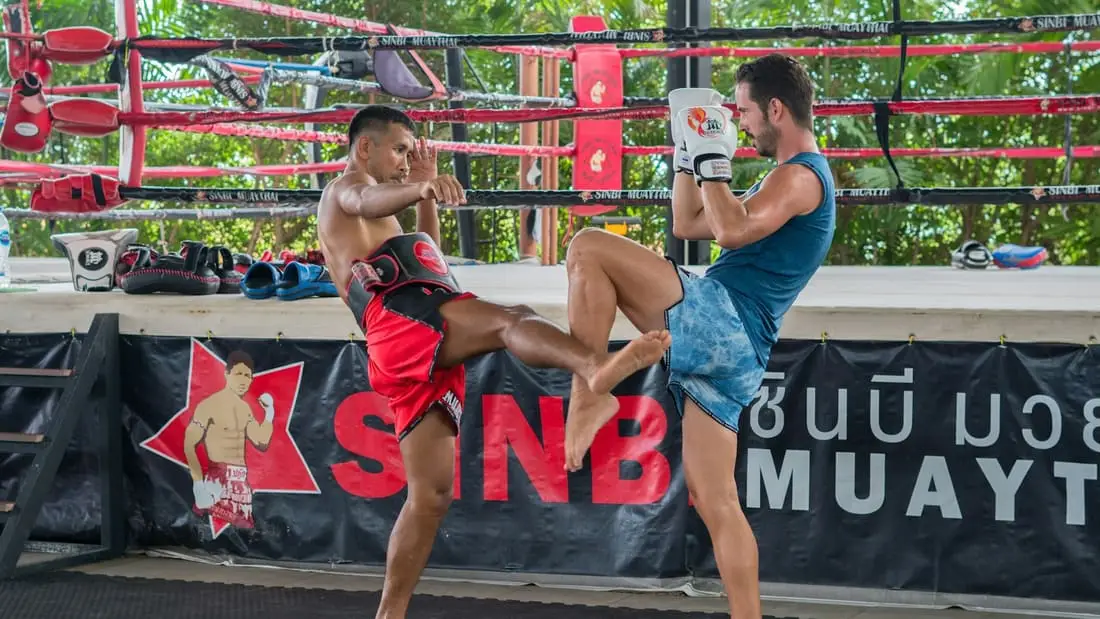 Séance d’entraînement de muay thai en plein air : un entraîneur tient les pattes d’ours, un pratiquant lance un coup de pied.