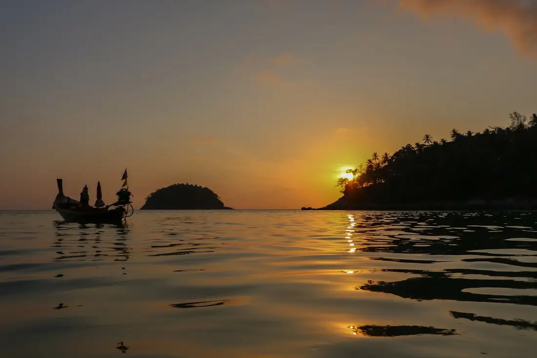 Coucher de soleil sur la plage de Kata, à Phuket, avec un bateau à longue queue en silhouette.