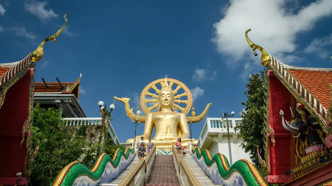 Le Big Buddha doré de Koh Samui au sommet de son escalier bordé de nagas, entre les pignons rouge et or du temple.
